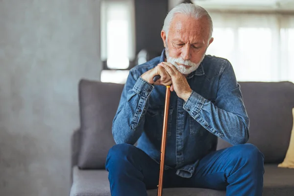Grey hair man with disabled stick sitting on sofa and thinking at home