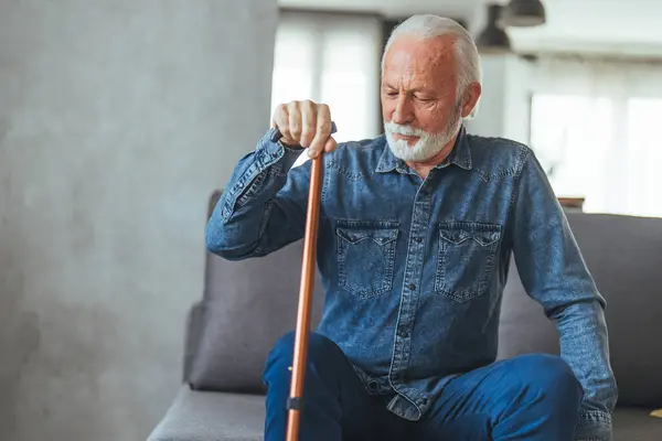 Senior man with disabled stick sitting on sofa at home