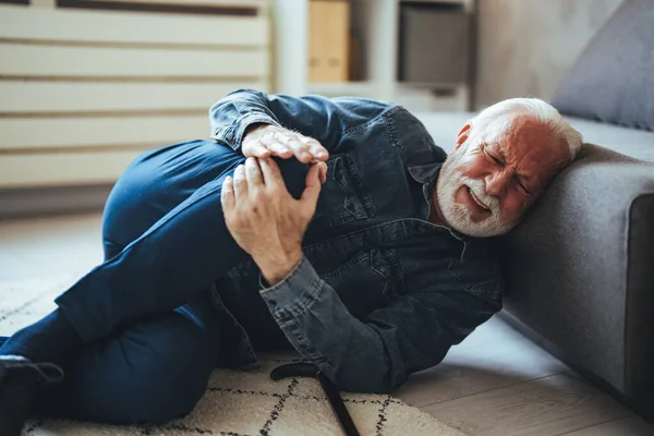 Senior caucasian man lying on on floor and suffering from pain near sofa at home
