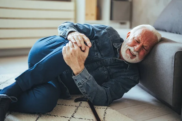 Senior caucasian man lying on on floor and suffering from pain near sofa at home