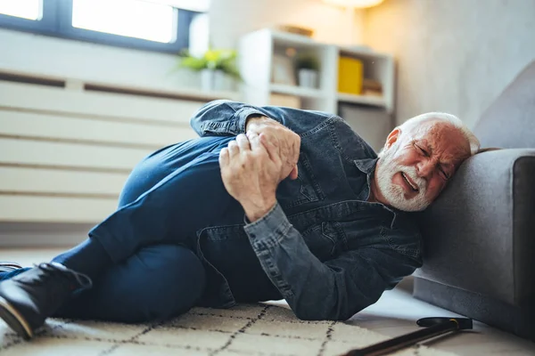 Senior caucasian man lying on on floor and suffering from pain near sofa at home