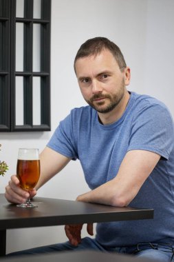 Sakallı genç bir adam kafedeki bir bardaktan bira içer.