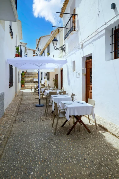 stock image A small cafe without people on a narrow street of the old town. White walls of houses and a street lined with pebbles.