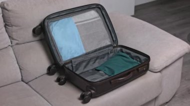 Yaz tatili için bavul hazırlıyorum. Kanepede bavulda dikkatlice toplanmış giysiler. Seyahat kavramı.
