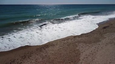 Kamera kumlu sahilden denize doğru hareket ediyor ve köpüğe dalıyor. Video 4K.