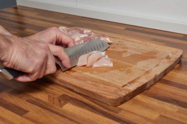 Erkek şef, ahşap tahtada tavuk dilimliyor. Aşçı bıçağıyla.