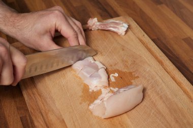 Erkek şef, ahşap tahtada tavuk dilimliyor. Aşçı bıçağıyla.