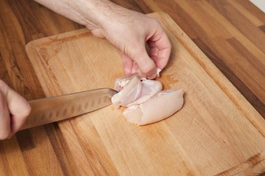 Erkek şef, ahşap tahtada tavuk dilimliyor. Aşçı bıçağıyla.