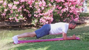 Şehir parkındaki bir paspasın üzerinde şınav çeken orta yaşlı bir sporcu. Spor salonu açık havada..