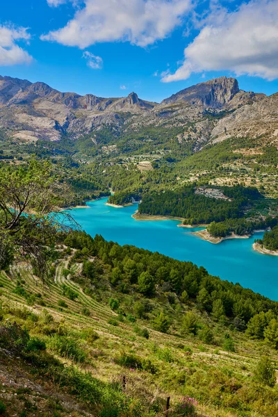 stock image Landscape of the Guadalest reservoir. Calm turquoise lake surrounded by rocky mountains with green trees located against blue sky in nature of Guadalest in in Alicante province of Spain