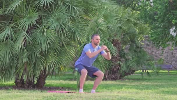 中年の白人男性が屋外の公園でフィットネスマットで座り練習をしています 健康的なアクティブライフスタイル — ストック動画