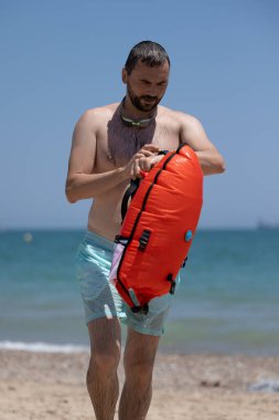 Kırmızı şamandıralı bir adam denizde yüzdükten sonra kıyıya geldi ve bir fitness nöbetinin sonucuna baktı..