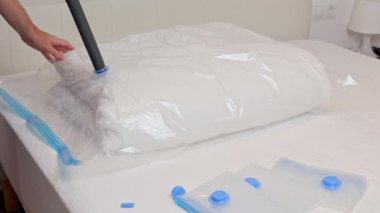 Elektrik süpürgesi ve kapakçık kullanarak battaniye ile sıkıştırma çantasından hava emen tanınmayan bir adamın görüntüsü. Yer saklama kavramı ve yatak depolama, depolama düzeni