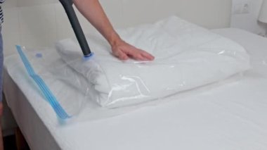 Elektrik süpürgesi ve kapakçık kullanarak battaniye ile sıkıştırma çantasından hava emen tanınmayan bir adamın görüntüsü. Yer saklama kavramı ve yatak depolama, depolama düzeni