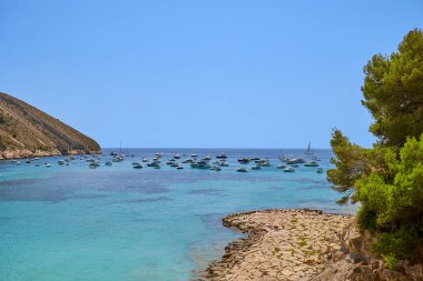 İspanya 'nın Costa Blanca bölgesi olan Cala El Portet olarak da bilinen temiz turkuaz suyla küçük körfeze demirlemiş yat ve tekne manzarası..