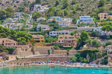 El Portet plajı, Moraira, Alicante, İspanya - 15 Ağustos 2023: Dağ yamacında küçük bir kasaba ve Akdeniz kıyısında güzel bir kumsal.