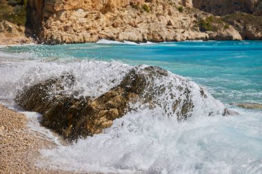 Dalgalar gün boyunca Akdeniz kıyılarında kayalara çarpıp çarpıyor. Cala del Moraig plajı Benitachell, Alicante, İspanya.