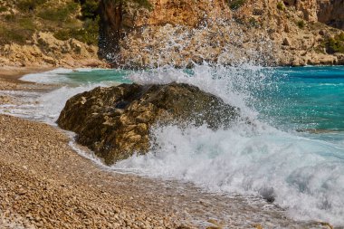 Dalgalar gün boyunca Akdeniz kıyılarında kayalara çarpıp çarpıyor. Cala del Moraig plajı Benitachell, Alicante, İspanya.