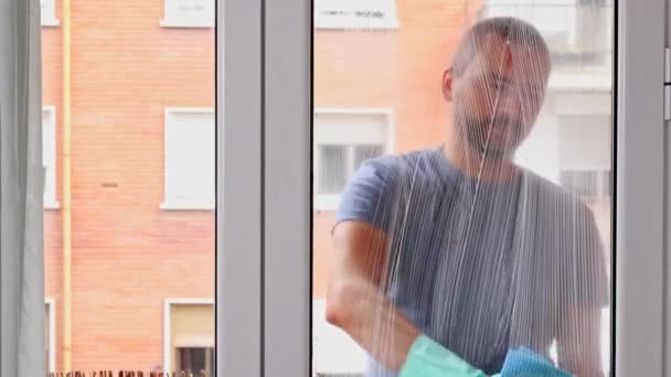 ハウスクリーニング ゴム製手袋の白人男性は特別な泡と青いナプキンを使用して窓のガラスをきれいにします — ストック動画