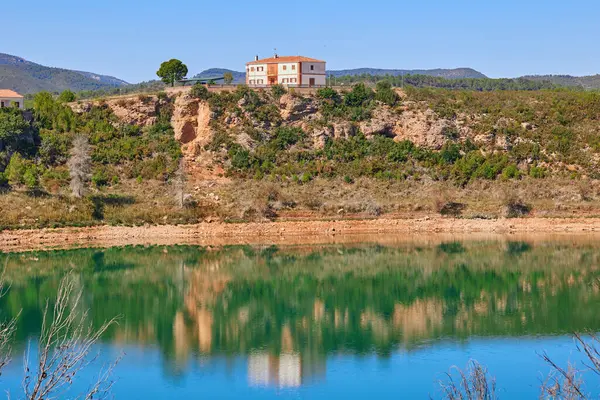 Building on the edge of Forata reservoir in Valencia region, Spain. The shore and the house are reflected on the surface of the water