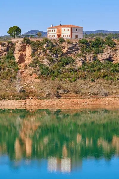Building on the edge of Forata reservoir in Valencia region, Spain. The shore and the house are reflected on the surface of the water