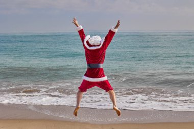 Sıcak bir yaz gününde Noel Baba denizde. Noel Baba, arkadan görülen, sahile doğru atlayan, denize bakan. Noel ya da sıcak ülkelerde yeni yıl tatili. Noel Baba 'nın yaz tatili.