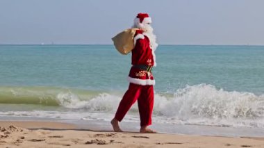 Omzunda hediyelerle dolu bir çantayla Noel Baba sıcak bir yaz gününde dalgalar boyunca kumlu sahil boyunca yürür. Sıcak ülkelerde Noel ya da yeni yıl tatili. Noel Baba 'nın yaz tatili.
