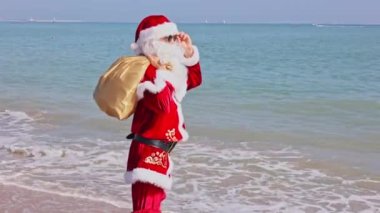 Omzunda hediyelerle dolu bir çantayla Noel Baba sıcak bir yaz gününde dalgalar boyunca kumlu sahil boyunca yürür. Sıcak ülkelerde Noel ya da yeni yıl tatili. Noel Baba 'nın yaz tatili.