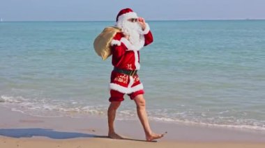 Omzunda hediyelerle dolu bir çantayla Noel Baba sıcak bir yaz gününde dalgalar boyunca kumlu sahil boyunca yürür. Sıcak ülkelerde Noel ya da yeni yıl tatili. Noel Baba 'nın yaz tatili.