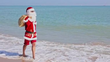 Omzunda hediyelerle dolu bir çantayla Noel Baba sıcak bir yaz gününde dalgalar boyunca kumlu sahil boyunca yürür. Sıcak ülkelerde Noel ya da yeni yıl tatili. Noel Baba 'nın yaz tatili.