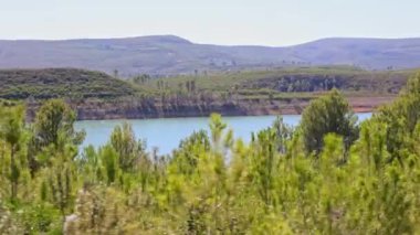 Rezervuar boyunca dağ yolunda araba kullanmak. Gölün yan penceresinden ve çevresini çevreleyen yeşil ağaçlarla kaplı dağlardan bak..