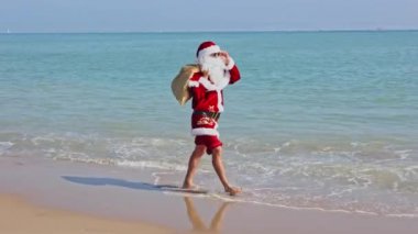 Omzunda hediyelerle dolu bir çantayla Noel Baba sıcak bir yaz gününde dalgalar boyunca kumlu sahil boyunca yürür. Sıcak ülkelerde Noel ya da yeni yıl tatili. Noel Baba 'nın yaz tatili.