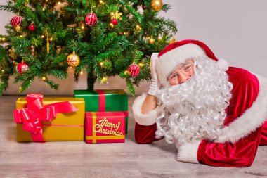 Noel Baba süslenmiş bir Noel ağacının altına Noel hediyesi koyar. Beyaz arkaplanda.