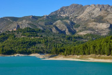 Dağın eteğindeki ormanla çevrili Guadalest rezervuarı turkuaz suyla çevrili güzel bir manzara. Guadalest, Valencia, İspanya.