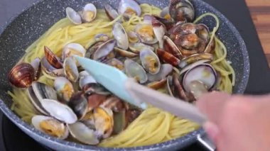 İstiridyeli geleneksel İtalyan deniz ürünleri makarnası pişiriyorum. Vongole usulü spagetti. Bir aşçı, spatulayla tavada kabuklu deniz ürünleriyle spagetti karıştırır..