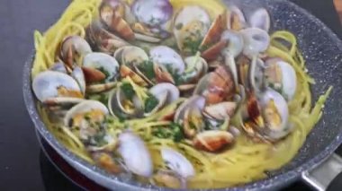 İstiridyeli geleneksel İtalyan deniz ürünleri makarnası pişiriyorum. Vongole usulü spagetti. Bir aşçı, spatulayla tavada kabuklu deniz ürünleriyle spagetti karıştırır..