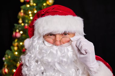 Noel Baba 'nın yakın portresi gözlüğünü ayarlıyor ve gözlüklerine bakıyor. Mutlu Noeller..