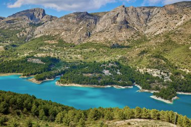 Guadalest rezervuarının manzarası. İspanya 'nın Alicante eyaletinde Guadalest' in doğasında mavi gökyüzüne karşı uzanan yeşil ağaçlarla çevrili sakin bir turkuaz gölü.