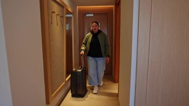 スーツケースを持った若い女性がホテルの部屋に入ります 彼はスーツケースを離れ 疲労からベッドに落ちる — ストック動画