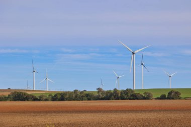 Mavi gökyüzünün altında tarımsal tarlaların olduğu rüzgar türbinleri. Yeşil enerji kavramı.