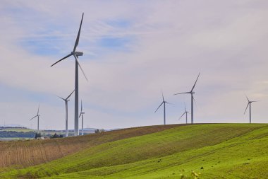 Mavi gökyüzünün altında tarımsal tarlaların olduğu rüzgar türbinleri. Yeşil enerji kavramı.