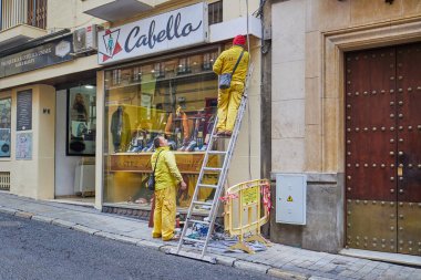 Sevilla, İspanya - 4 Ocak 2024: Sarı üniformalı iki işçi bir binanın ön cephesini onarıyor.