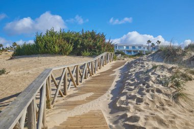 Cadiz, İspanya - 4 Ocak 2024: Kumsaldan sahil evine giden ahşap patika yol, kum tepeleri ve çalılarla kaplı..