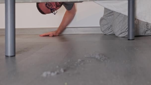 男は多くの塵が蓄積したベッドの下を見ます — ストック動画
