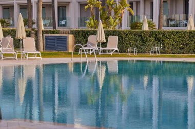 Güneş şezlongları ve şemsiyeli boş yüzme havuzu.