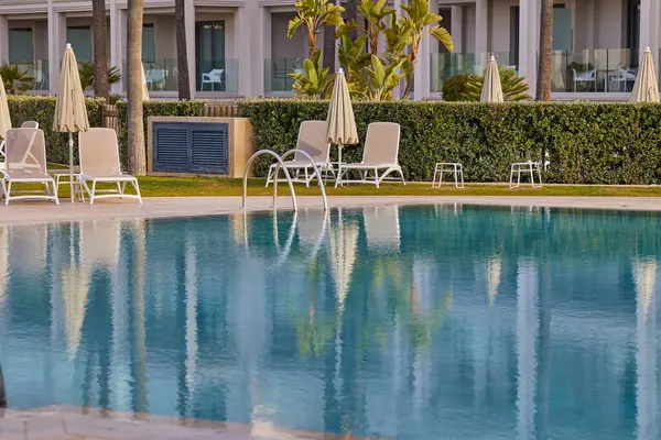 Güneş şezlongları ve şemsiyeli boş yüzme havuzu.