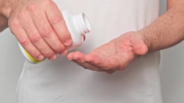 一个穿着白色T恤的年轻人把药丸倒进了他的手里 欧米茄3金鱼油胶囊 白色背景的特写 — 图库视频影像