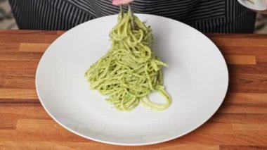Bir kadın elinin tabağa pesto soslu spagetti koyarkenki yakın çekimi.