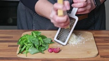 Pesto sosu pişirmek. Kadın eli, parmesan peynirini rendeliyor..