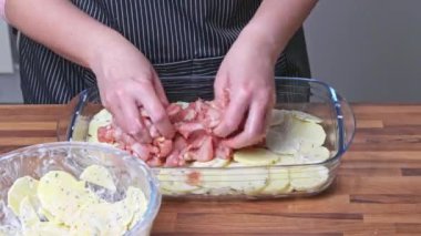 Kadın cam bir tabakta patates katmanına tavuk eti koyar. Evde yemek pişirmek..